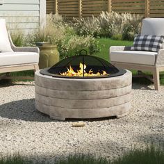 a fire pit sitting in the middle of a gravel field next to two chairs and a table