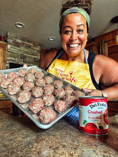 a woman holding a pan full of meatballs next to a can of canned milk