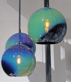 two blue and green glass balls hanging from a metal pole with one light on it