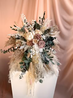 a white vase filled with flowers and greenery on top of a table next to a pink wall