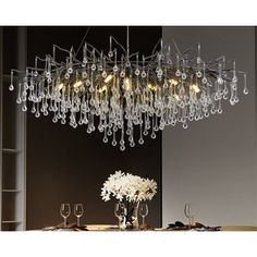 a chandelier hanging over a dining table with wine glasses and flowers on it