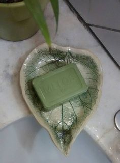 a green soap bar sitting on top of a leaf shaped bowl next to a plant