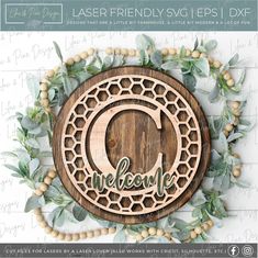 laser - engraved wooden circle with the word welcome surrounded by greenery and wood beads