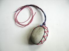 a rock with red string attached to it sitting on a white surface next to a cord