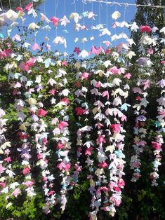 some pink and white paper cranes hanging from a wire in front of green trees with blue sky