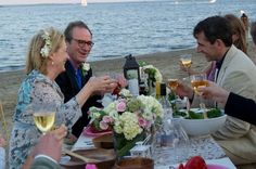 a group of people sitting at a table with wine glasses in front of the ocean