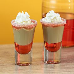 two shot glasses filled with chocolate and whipped cream sitting on top of a wooden table