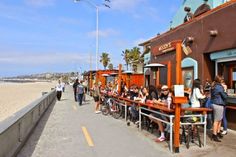 people are sitting at tables on the boardwalk by the beach in front of a restaurant