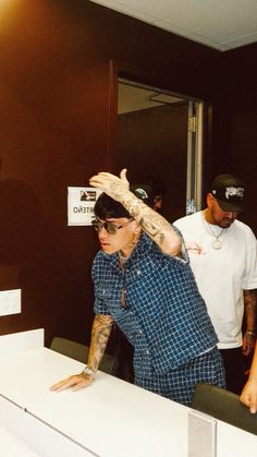 a man with tattoos on his arm standing in front of a counter and another man behind him