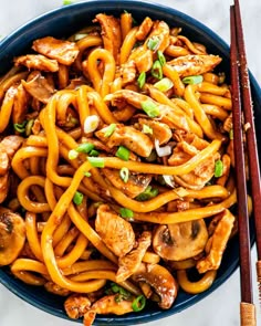 a blue bowl filled with chicken and noodles next to chopsticks on a white table