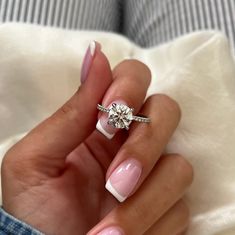 a woman's hand with pink and white manicured nails holding a diamond ring