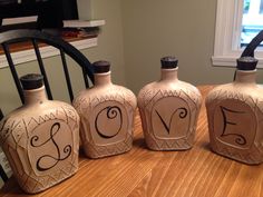 four vases sitting on top of a wooden table in front of a window with the word love painted on them