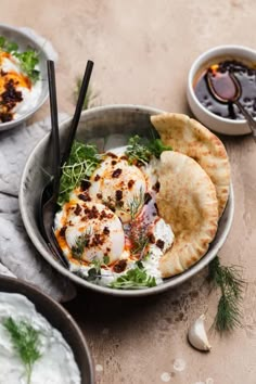 two bowls filled with food on top of a table next to some dipping sauces