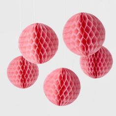 three pink honeycombs hanging from strings in front of a white wall and ceiling