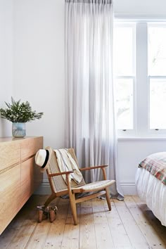 a bed room with a neatly made bed next to a window and a chair in front of it