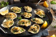 a pan filled with oysters on top of a table next to lemon wedges