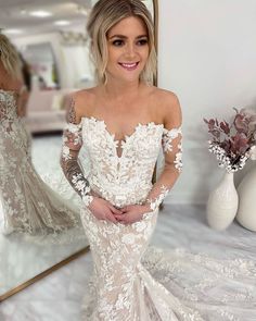 a woman in a white wedding dress standing next to a mirror with her hands on her hips