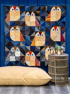 a blue wall with an owl quilt on it next to a pillow and bird cage