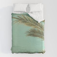 a bed covered in a green comforter with palm leaves on the pillow and two pillows