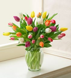 a green vase filled with lots of colorful tulips