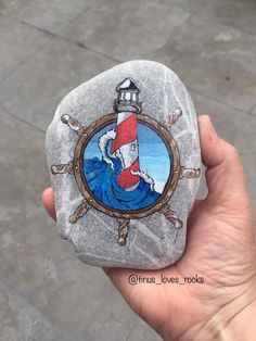 a hand holding a painted rock with a lighthouse on it