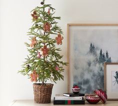 a small christmas tree sitting on top of a wooden table next to a basket filled with ornaments