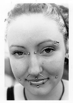 a black and white photo of a woman with piercings on her nose