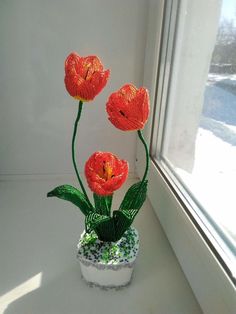 three red flowers sitting in a white vase on a window sill next to a snow covered ground