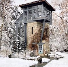 an old stone building with a blue door and window in the middle of snow covered trees