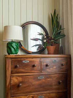 a wooden dresser with a mirror and potted plants on top, along with a lamp