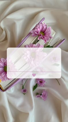 an open book sitting on top of a bed covered in white sheets and pink flowers