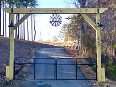 an open gate with a windmill in the background on a dirt road surrounded by trees