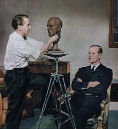 two men standing next to each other in front of a statue on a tripod