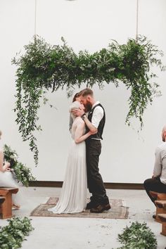 a bride and groom kissing in front of an arch of greenery at their wedding ceremony