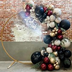 a christmas wreath made out of balloons and other holiday decorations on a circular stand in front of a brick wall