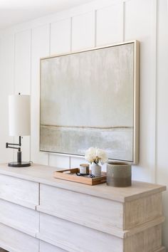 a white dresser with flowers on it and a large painting hanging above the top shelf