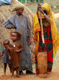 three women and two children standing in front of a straw hut