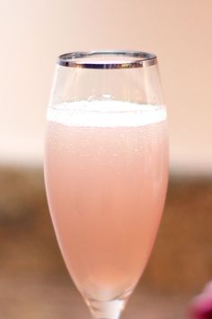 a glass filled with liquid sitting on top of a wooden table next to a pink flower