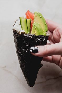 a hand holding a piece of sushi with cucumber, avocado and carrots