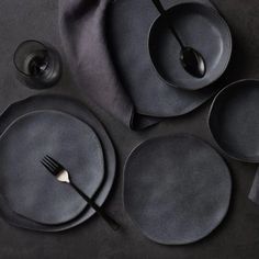 an assortment of black plates and utensils on a dark surface with napkins