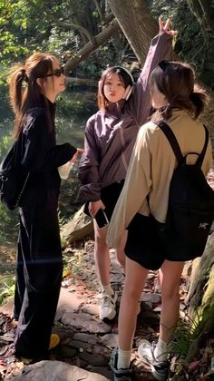 three young women standing on a path in the woods, one pointing at something while the other holds her hand up