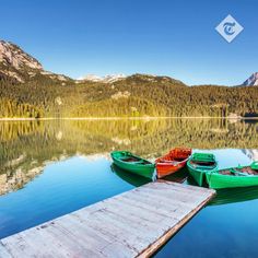 three boats are docked at the end of a pier on a lake with mountains in the background