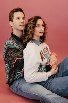 a man and woman are sitting on the floor posing for a photo in front of a pink background