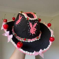 a woman's hand is holding a black hat with pink decorations and cherries