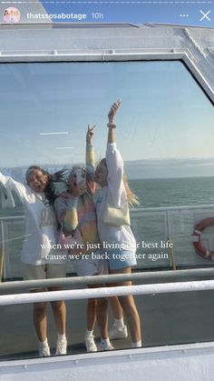 three girls are standing on the deck of a boat with their arms in the air