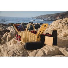 a picnic basket sitting on top of a rock next to the ocean with other items in it