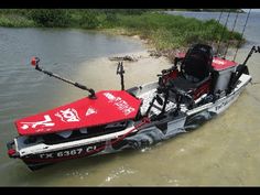 a red and black boat is sitting in the water with two fishing rods attached to it