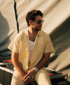 a man sitting on top of a wooden bench next to a white sheet covered wall