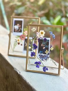 two gold frames with flowers and photos in them sitting on a stone ledge next to trees