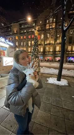 a woman is walking down the street with her dog and holding a fake christmas tree